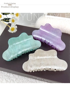 Close-up of three wavy cloud hair claws in pearlescent green, purple, and beige finish