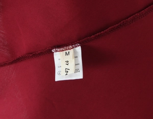 Détail de l'étiquette de taille M et instructions de lavage sur robe rouge foncé