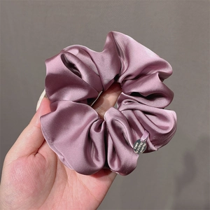Dusty pink satin scrunchie with silk texture and metal tag shown on a neutral background