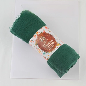 Dark green crinkle cotton linen scarf with frayed edges on a minimalist background