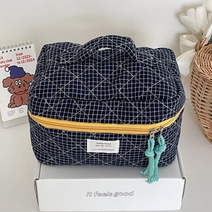 Detail of navy blue plaid quilted makeup bag with handle and double yellow zippers