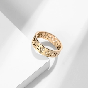Macro detail of golden Viking rune cutout ring on a minimalist white platform