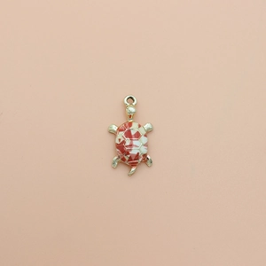 Macro view of cartoon turtle alloy pendant with red and white enamel on pink background
