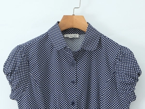 Detail of blue polka dot blouse with puff sleeves and collared neckline on hanger