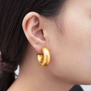 Close-up of golden hammered C-shaped hoop earrings on female model's ear