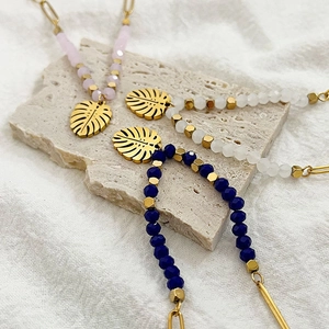 Bohemian beaded necklace with 18k gold monstera leaf pendant shown on stone display