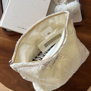 Détail d'une trousse à maquillage en dentelle fleurie montrant sa capacité de rangement