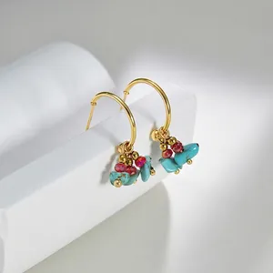 Detail of gold hoop earrings featuring turquoise stones and red beads on a minimalist stand