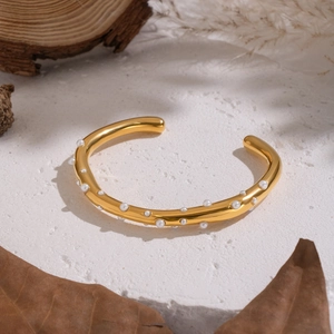 Gold plated stainless steel open bangle with white pearls on a textured stone surface