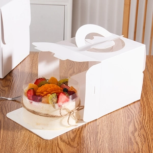 White birthday cake box with handle and clear window featuring fresh fruit cake on wood
