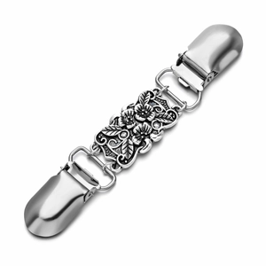 Detailed macro view of vintage silver cardigan clip with floral pattern on white background