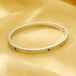 Detailed close-up of a silver evil eye bangle with crystals on a luxury gold satin background