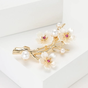 Elegant gold flower brooch with white shell petals and pearls on a white podium