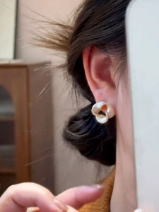 Macro view of 14K gold plated flower earrings with white inlay worn on the ear