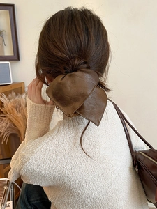 Detail of dark brown leather bow hair tie worn on hair, showing soft texture and style
