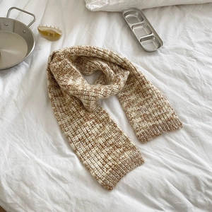 Detailed knit texture of beige and brown blend scarf on a soft white fabric surface