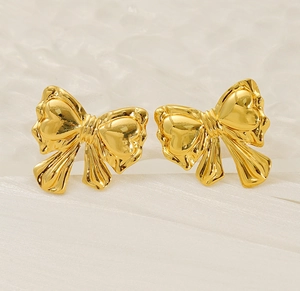 Macro shot of 3D golden bow stud earrings on luxury white silk background with ripples