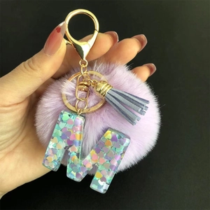 Détail du porte-clés lettre M en résine avec pompon violet et frange bleue