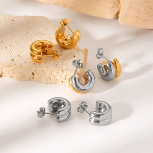 Macro detail of chunky gold and silver hoop earrings on a minimalist stone background