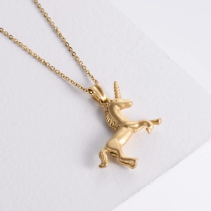 Minimalist gold unicorn pendant necklace with a matte sandblasted finish on white surface
