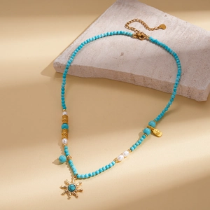 Gros plan sur collier de perles et turquoise avec pendentif soleil et bijoux dorés