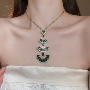 Macro detail of cascading fan-shaped emerald green pendants on a gold tassel necklace