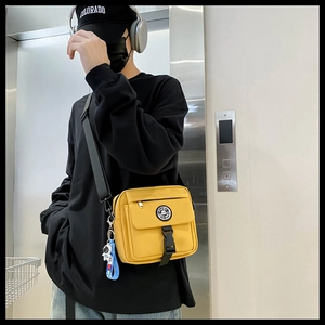 Detail of yellow nylon crossbody bag with astronaut charm and adjustable strap shown on model