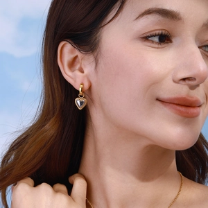 18k gold plated heart drop earrings with beaded bezel shown on a model against blue sky