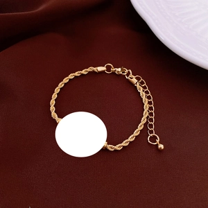 Detail of gold twisted rope chain bracelet with a blank round charm on a brown fabric