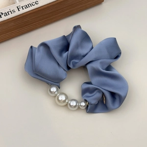 Detailopname van een blauwe satijnen scrunchie met elegante witte parels op een zachte basis