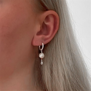 Detail of twisted silver hoop earrings with white pearl and small star disc on model