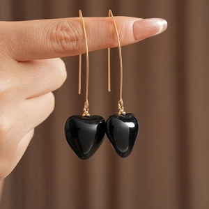 Detailed view of long gold drop earrings with black heart-shaped vintage pendants