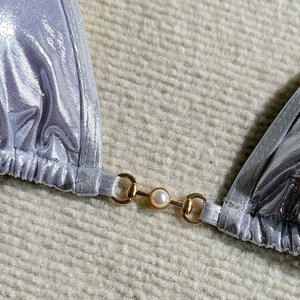 Macro detail of silver metallic bikini fabric with gold horsebit pearl buckle