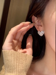 Close-up of heart-shaped silver earrings with sparkling cubic zirconia on model's ear