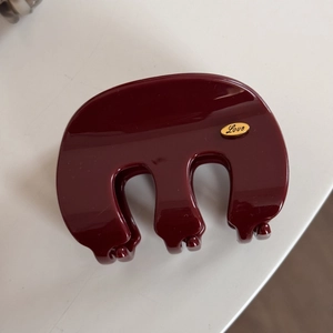 Close-up of deep red hair claw clip with golden Love label on smooth resin surface