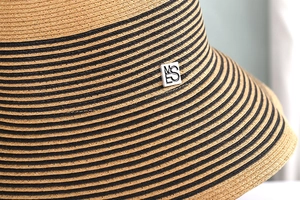 Close-up of contrast striped straw sun hat with detailed weave and metal logo plaque