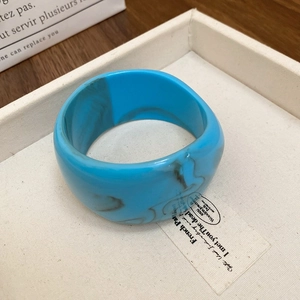 Detail showing the blue marble texture of a wide resin bangle on a minimalist tray