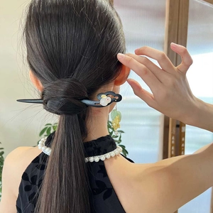 Détail d'un pic à cheveux en bois avec lapin blanc et pompon floral vert en chignon