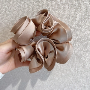 Detailed view of champagne satin scrunchie with elegant ruffled texture and soft silk sheen