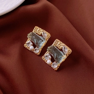 Detailed shot of gold-plated geometric stud with blue gemstone and pearls on satin