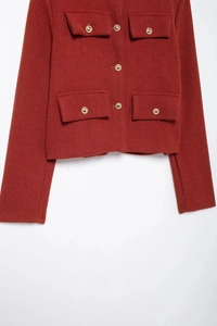 Détail de la veste en maille rouge brique avec boutons dorés et texture de tissu tissé