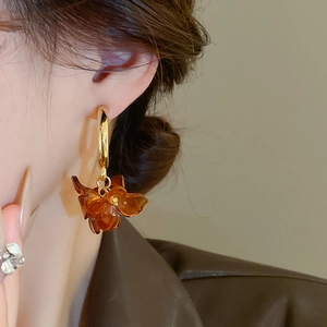 Close-up of amber flower drop earring with gold ring worn by model in warm lighting
