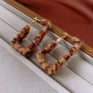 Macro detail of square leopard print earrings with flocked texture and gold metal hooks
