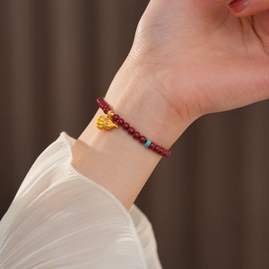 Detail of beaded cinnabar bracelet with gold gourd pendant on woman wrist