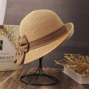 Detail view of woven straw sun hat featuring a large brown bow on a vintage display stand