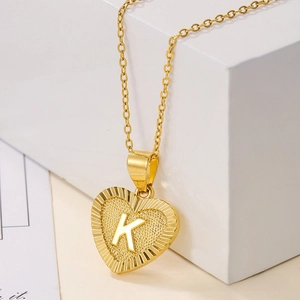 Detail of gold heart pendant necklace with sunburst texture and engraved letter K