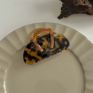 Close-up of a semi-circular dark leopard print hair claw clip on a white wavy ceramic plate