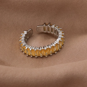 Detail of silver open ring featuring a row of square-cut yellow zircon stones on brown fabric