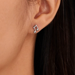 Close-up detail of a minimalist silver music note stud earring worn by a model