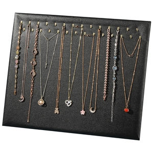 Black jewelry display board with gold metal hooks showcasing multiple necklaces and bracelets